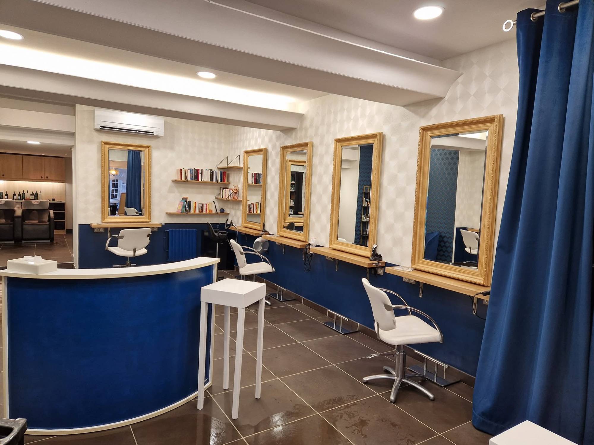 Intérieur du salon Cosy Coiffure : comptoir d'accueil bleu, fauteuils blancs et miroirs dorés